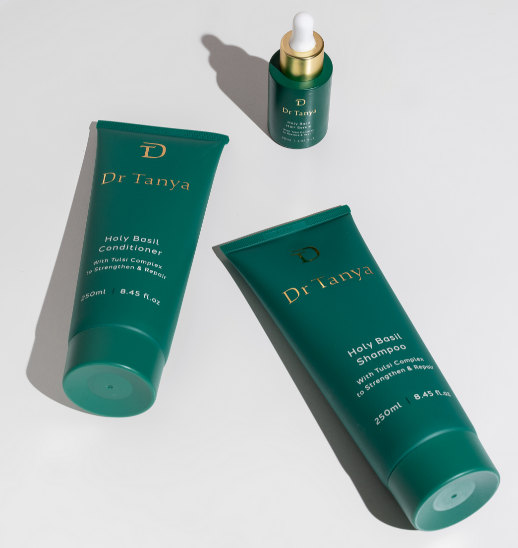 Two green bottles of Holy Basil shampoo and conditioner lying next to a small bottle of hair serum