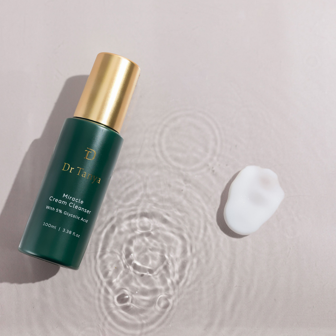 A bottle of face cleanser lying face-up in a pool of water with a drop of cleanser next to it