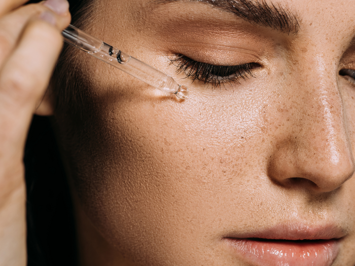 A close up photo of a woman applying a serum dropper to her face