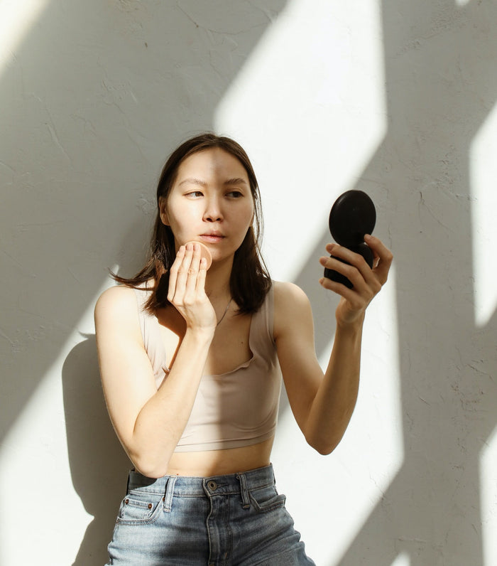 A lady applying make up while looking at herself in the compact mirror