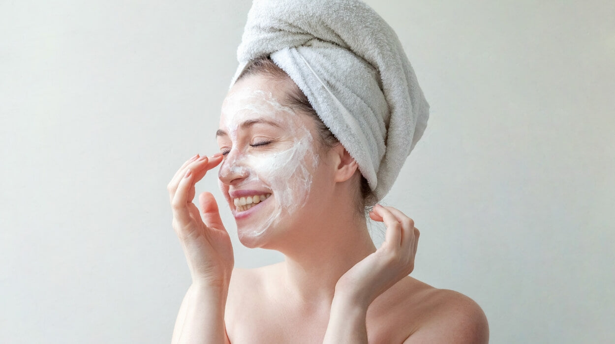 A woman wearing a hair towel applies a face mask