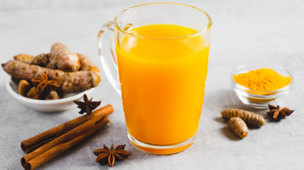 A glass of juice with turmeric, ginger and cinnamon around it