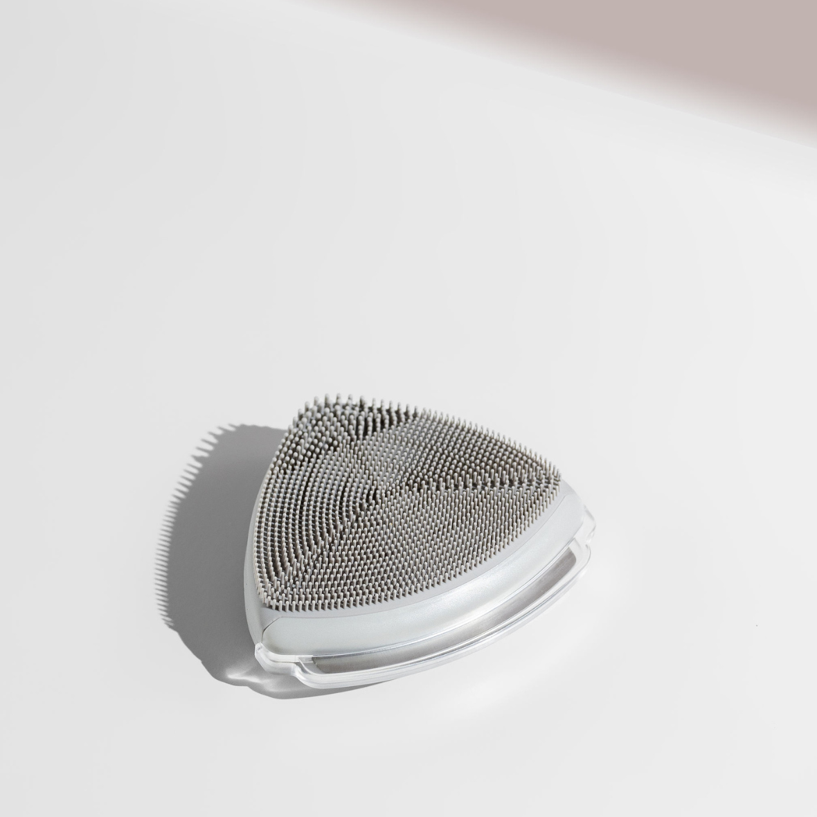 A triangular white and grey face exfoliator device on a white surface