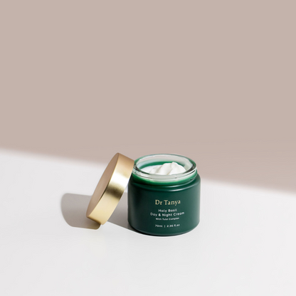 An opened dark green tub of face cream with the gold lid propped against it