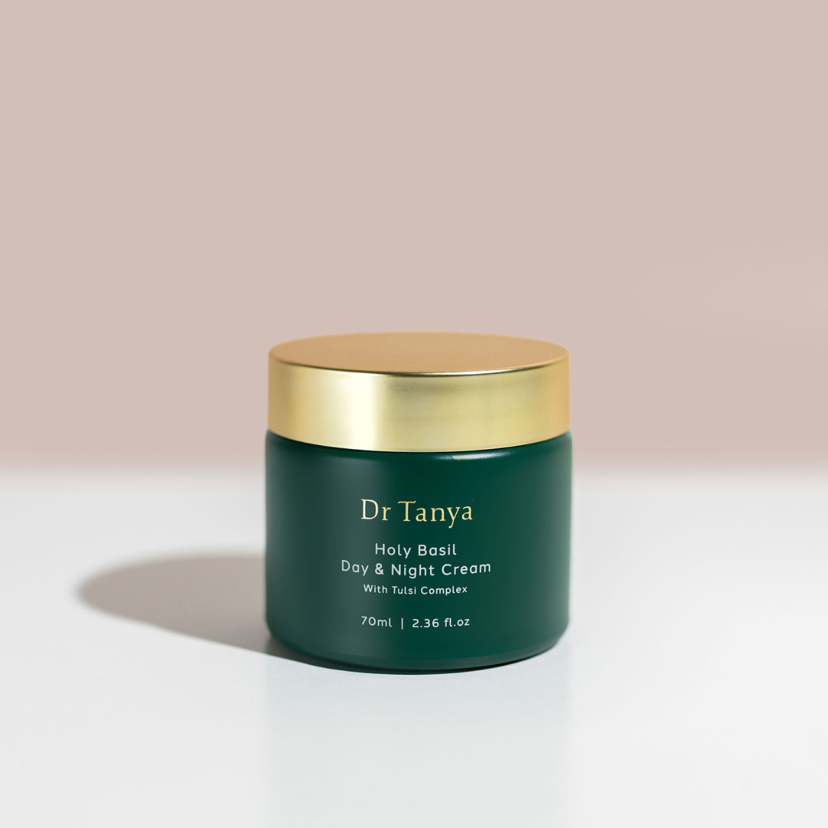 A round green pot of day and night cream with a gold lid against a pink backdrop