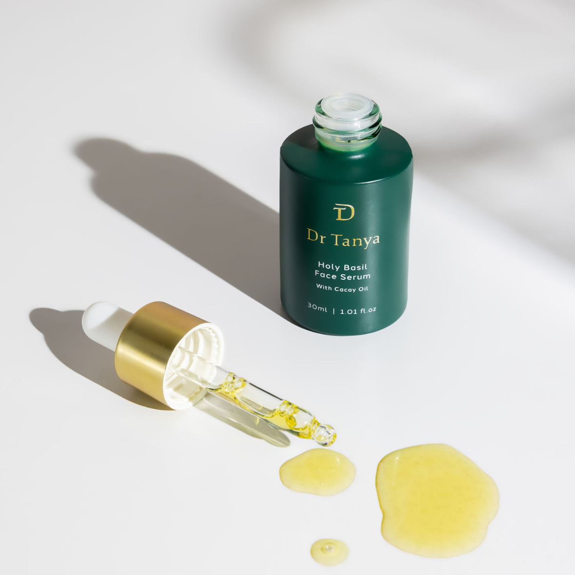 Drops of golden face serum next to a green bottle and dropper