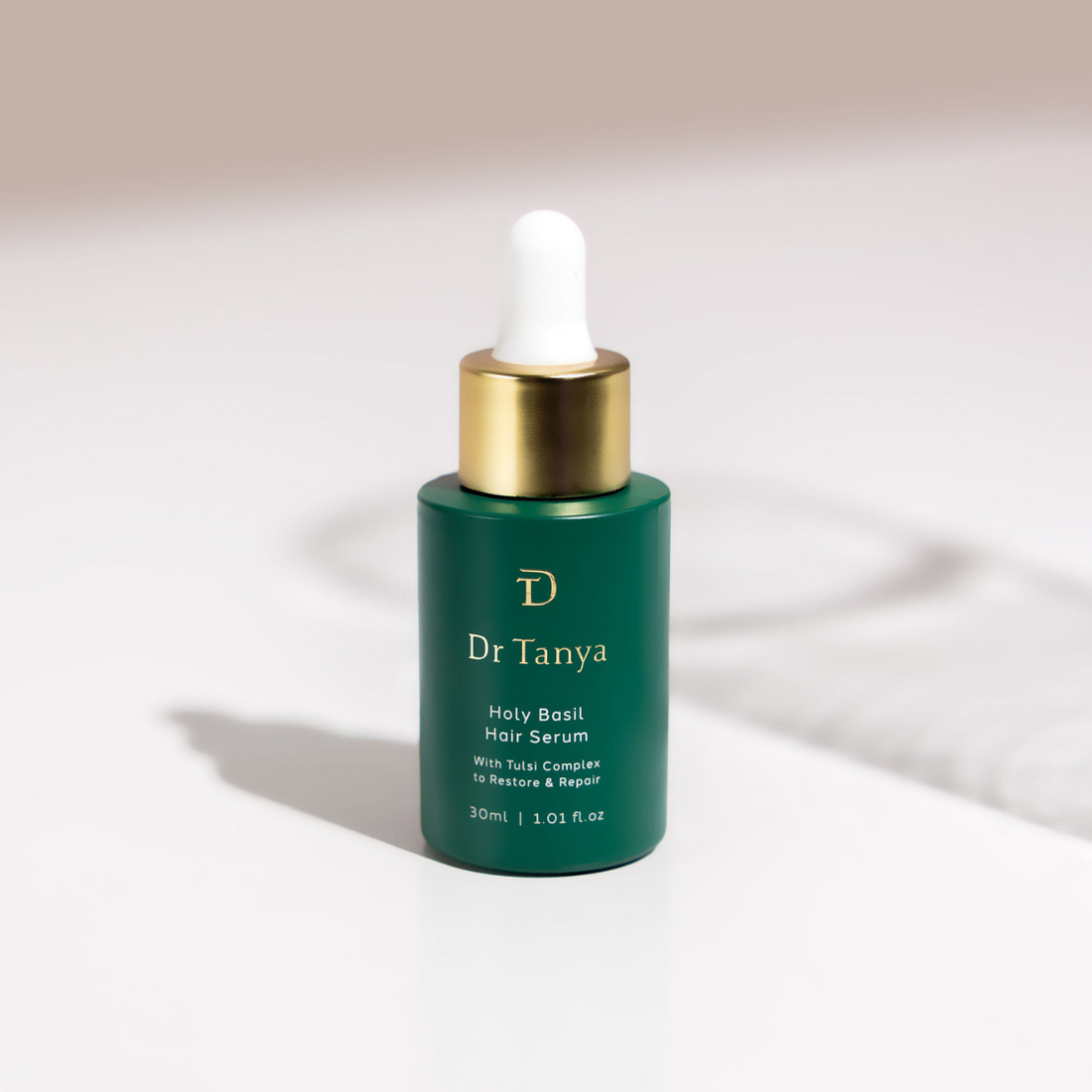 A green bottle of hair serum on a white surface with shadows cast