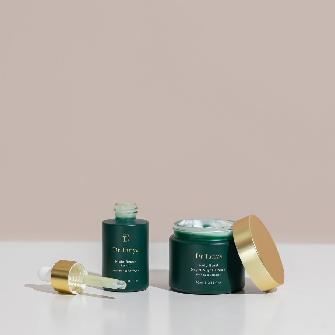 Two deep green bottles of face product with their gold lids off set against a pale pink background
