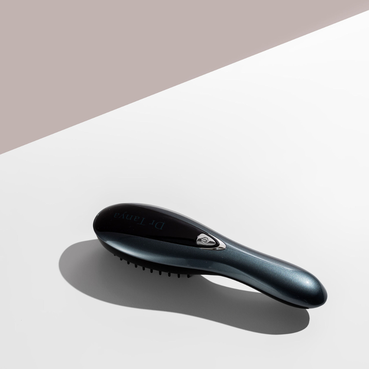 A black vibrating hair brush lying face down on a white surface