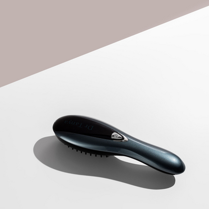 A black vibrating hair brush lying face down on a white surface