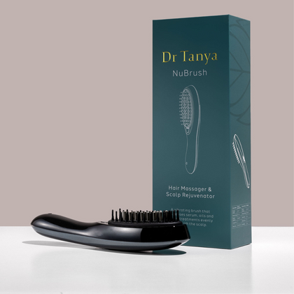 A black hair massager brush lying next to a green box