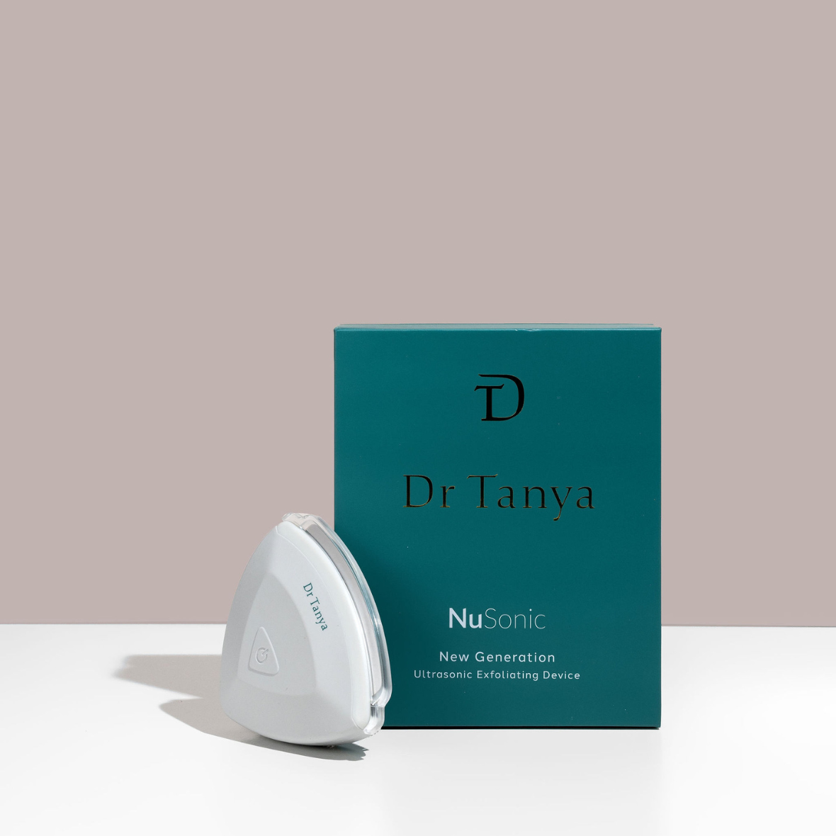 A white triangle-shaped face exfoliating device propped against a green box with gold and white text