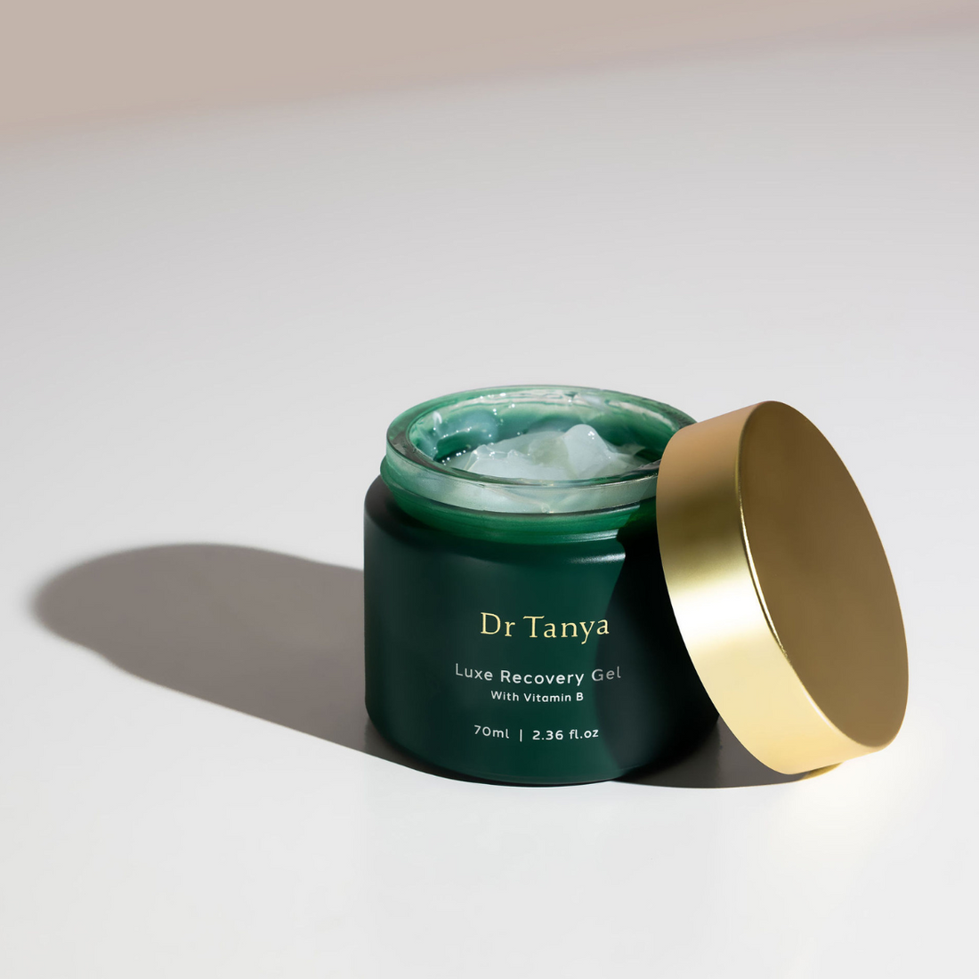 An emerald coloured pot of facial gel with a gold lid propped against it