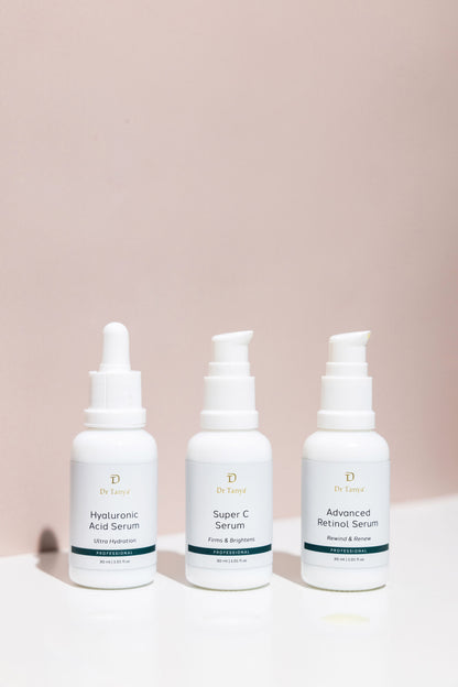 Three white bottles of face serum in front of a blush pink wall